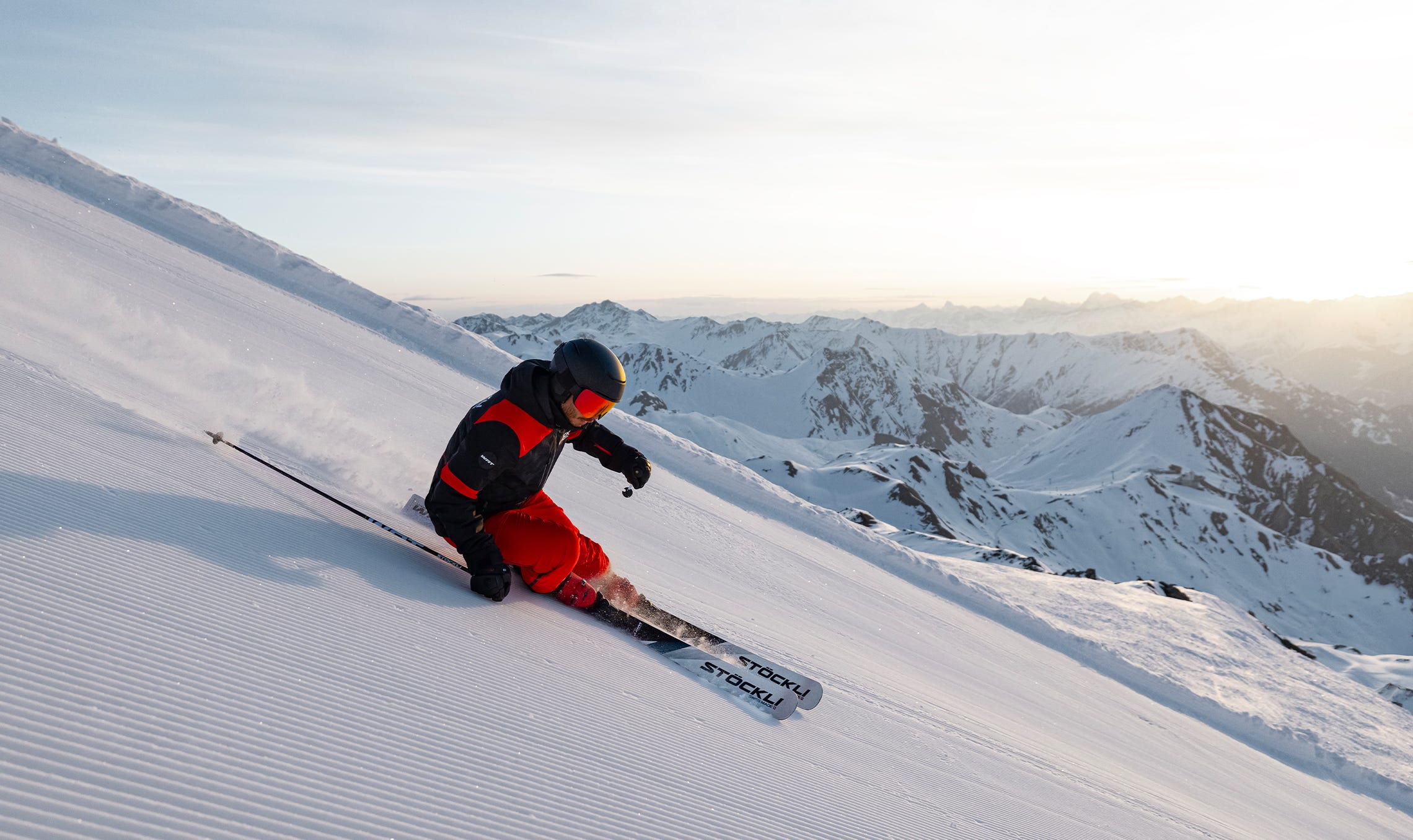 Stöckli Skifahrer carvt bei Sonnenaufgang über eine frisch präparierte Piste