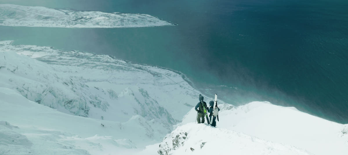 Freeriderin zieht einen Schwung durch tiefen Pulverschnee, im Hintergrund verschneite Felsen