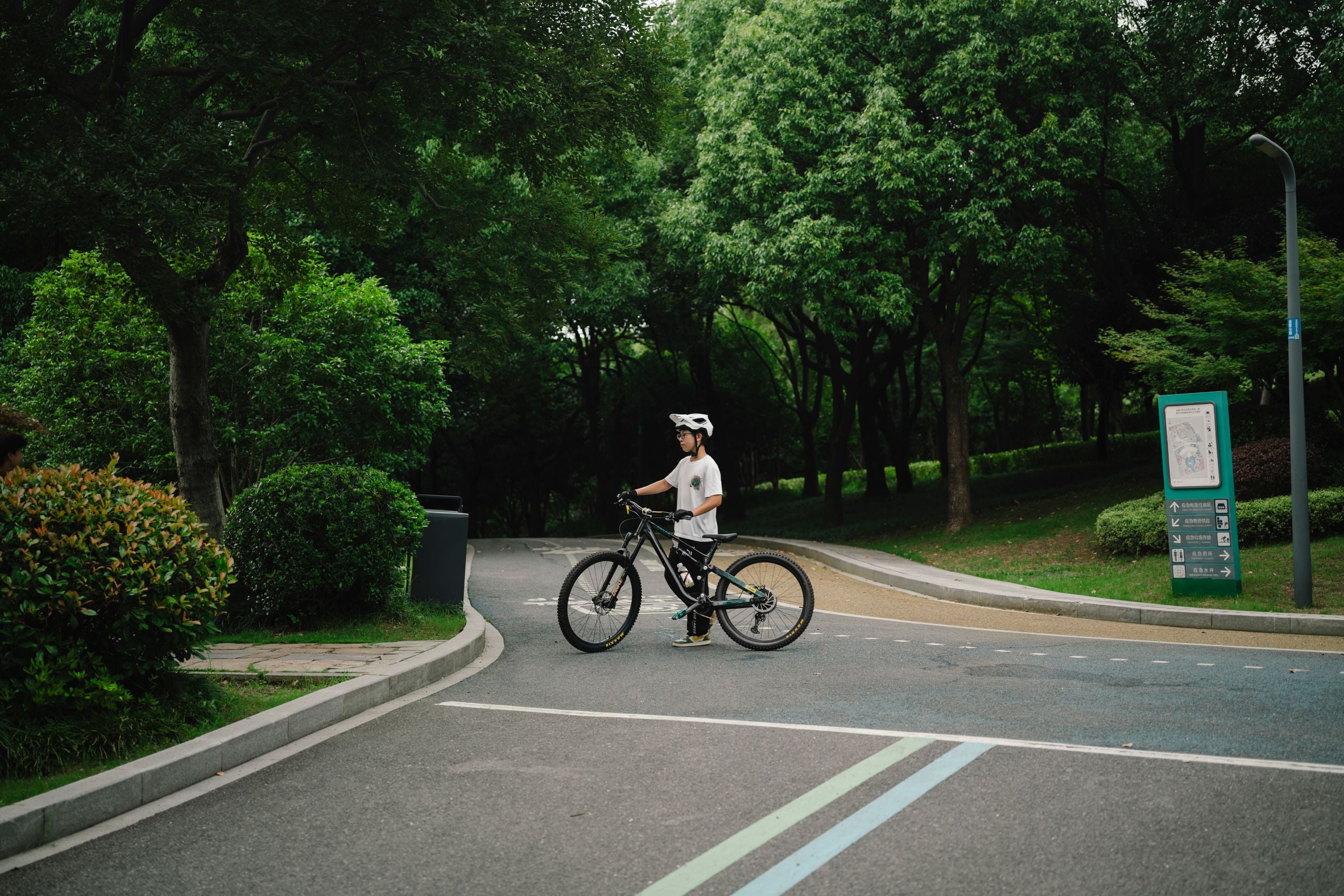 Kind mit Fahrradhelm auf einem Fahrrad an einem grünen Parkweg
