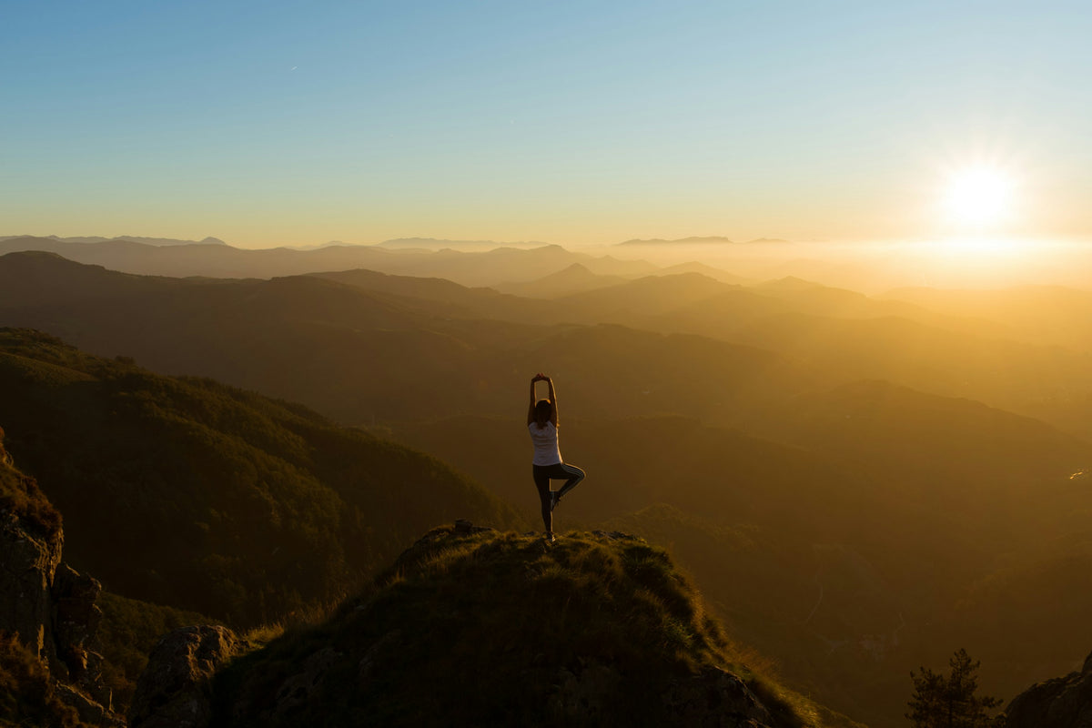 Frau in einer Yogapose auf einem Berggipfel im warmen Abendlicht
