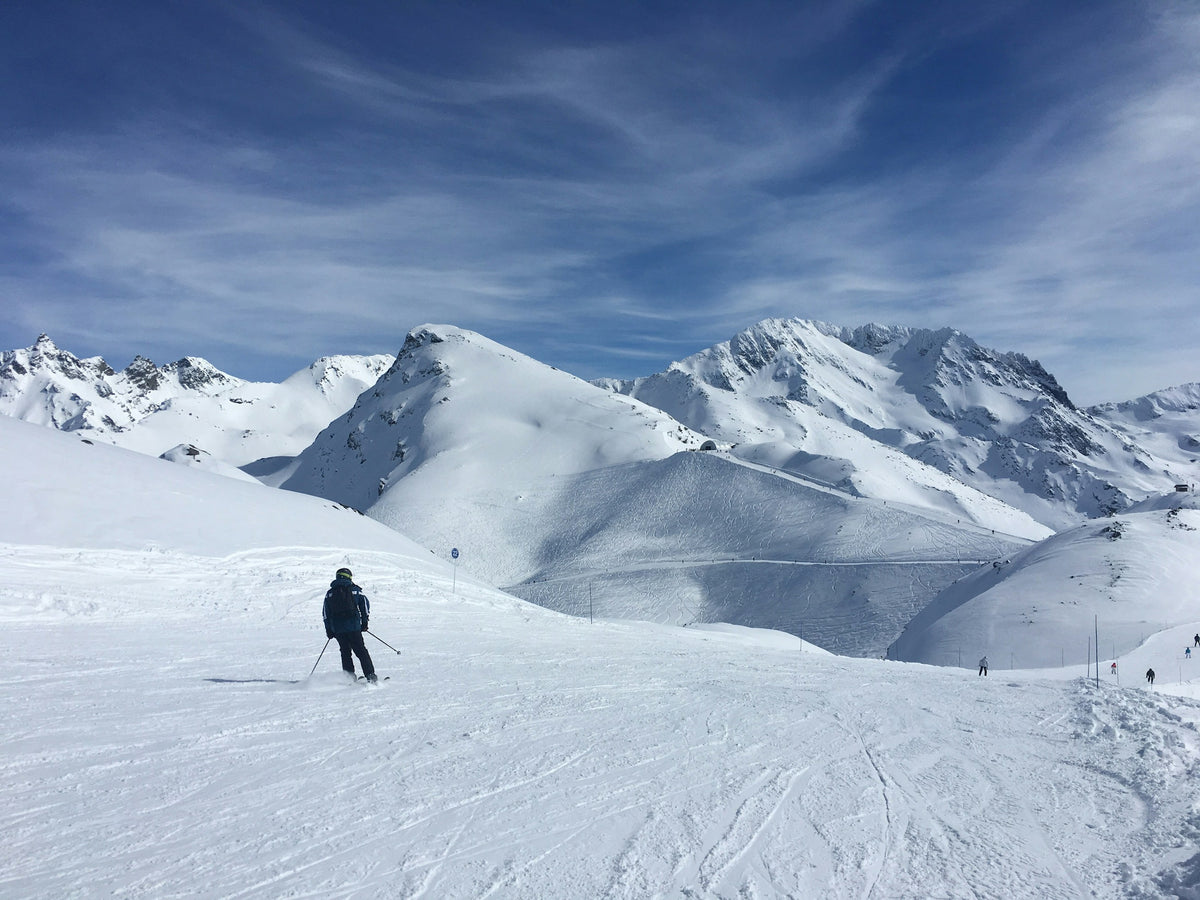 Skifahrer auf einer weiten Piste vor den verschneiten Bergen der französischen Alpen.