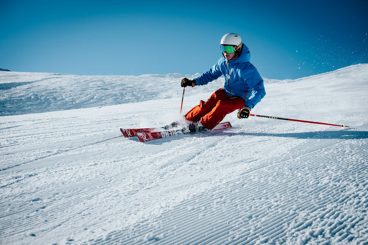 Skifahrer in blauer Jacke fährt einen Carvingschwung auf einer frisch präparierten Piste.