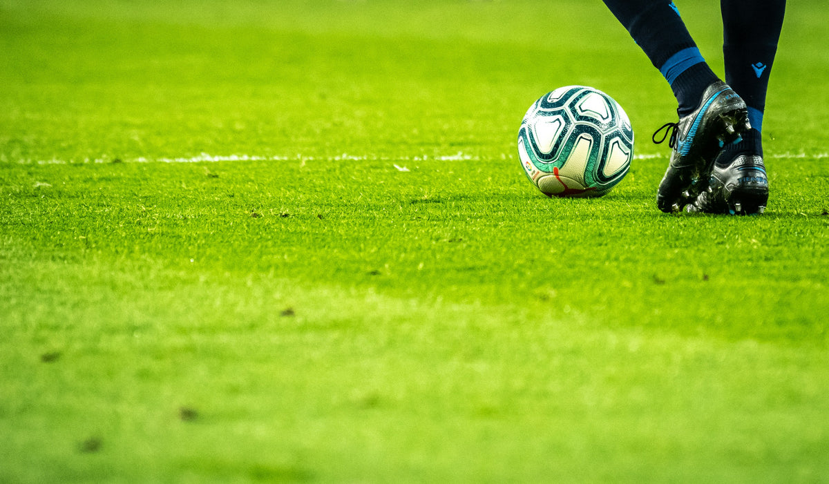 Fußball und Fußballschuhe auf einem grünen Spielfeld