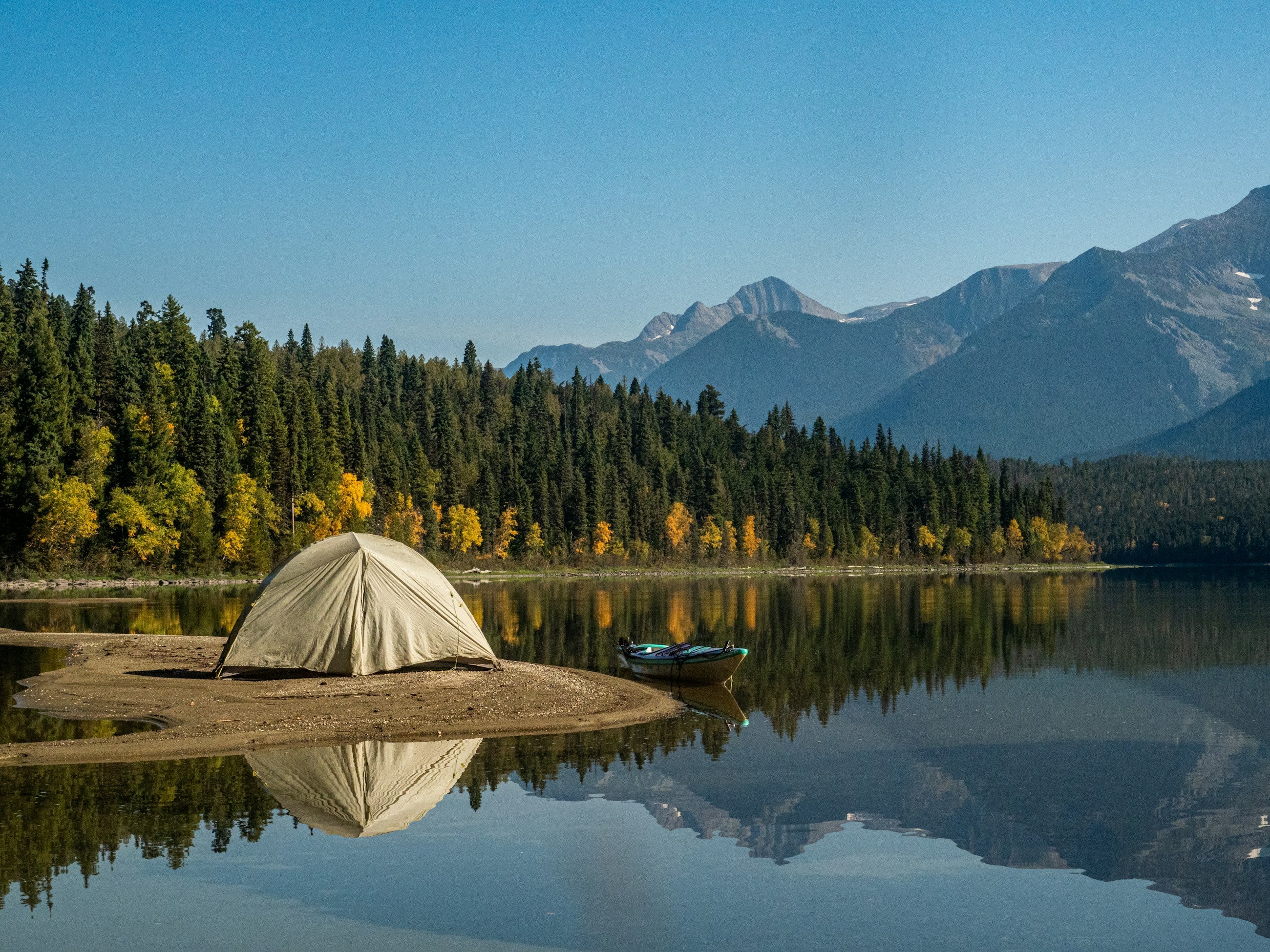 Zelt am ruhigen Bergsee mit Wald und Gebirgspanorama