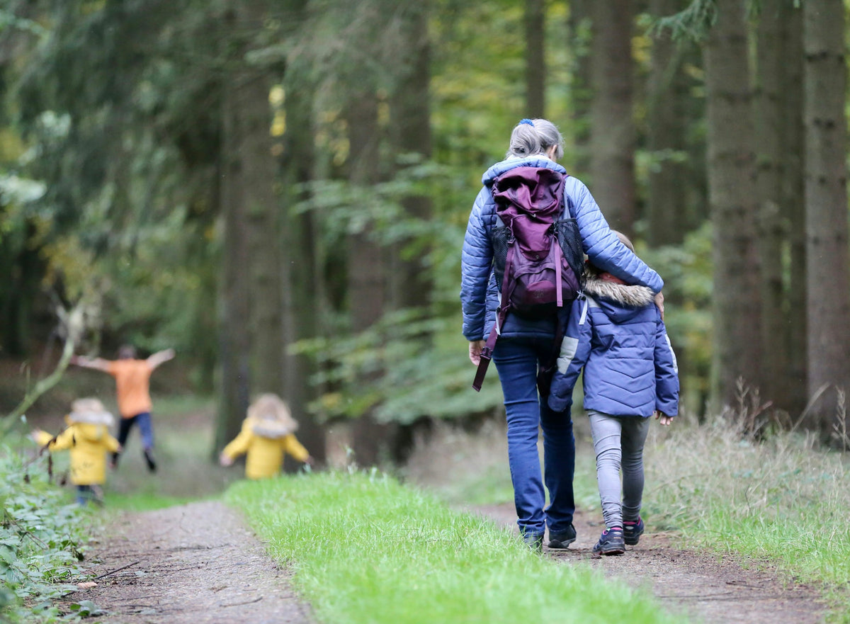 Erwachsene und Kinder mit Rucksäcken beim Wandern auf einem Waldweg
