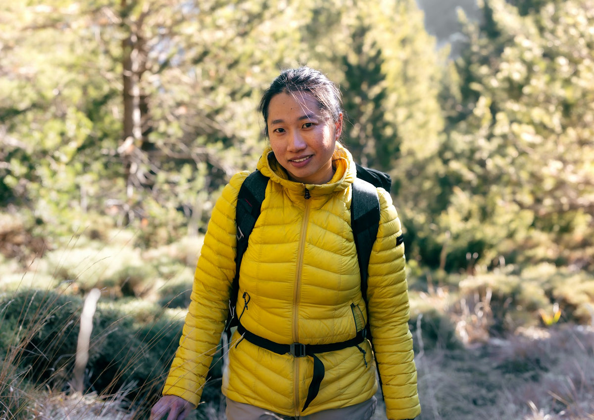 Wanderin in gelber Daunenjacke im Bergwald